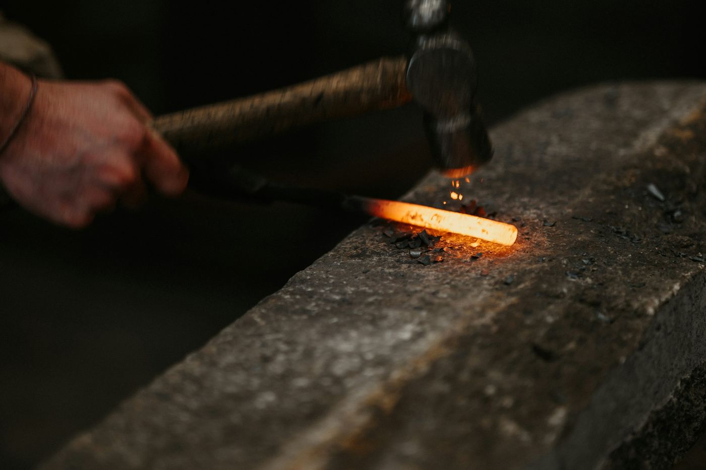 A hammer striking glowing steel on an anvil