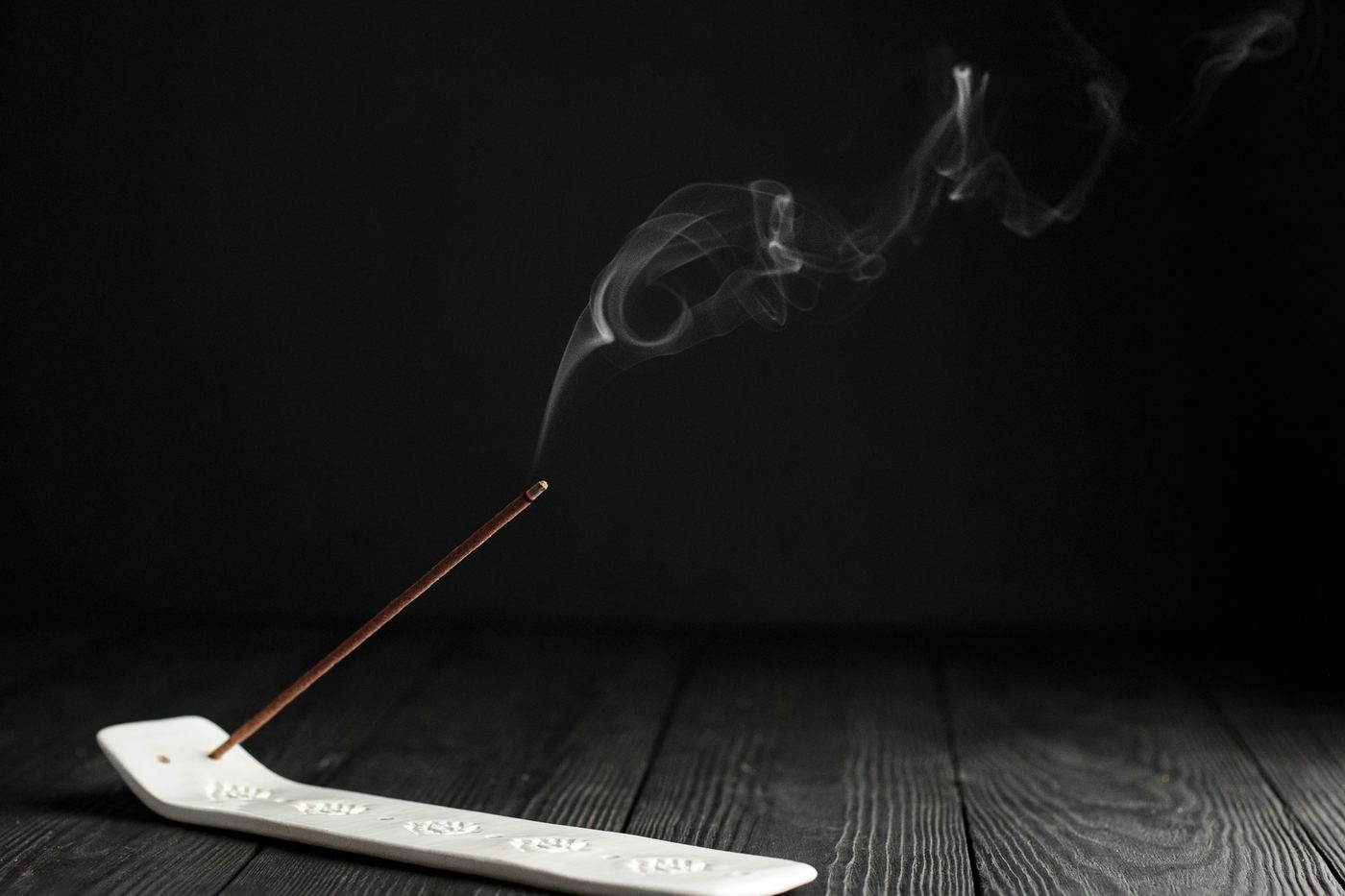 A stick of incense smoking on a dark wooden floor