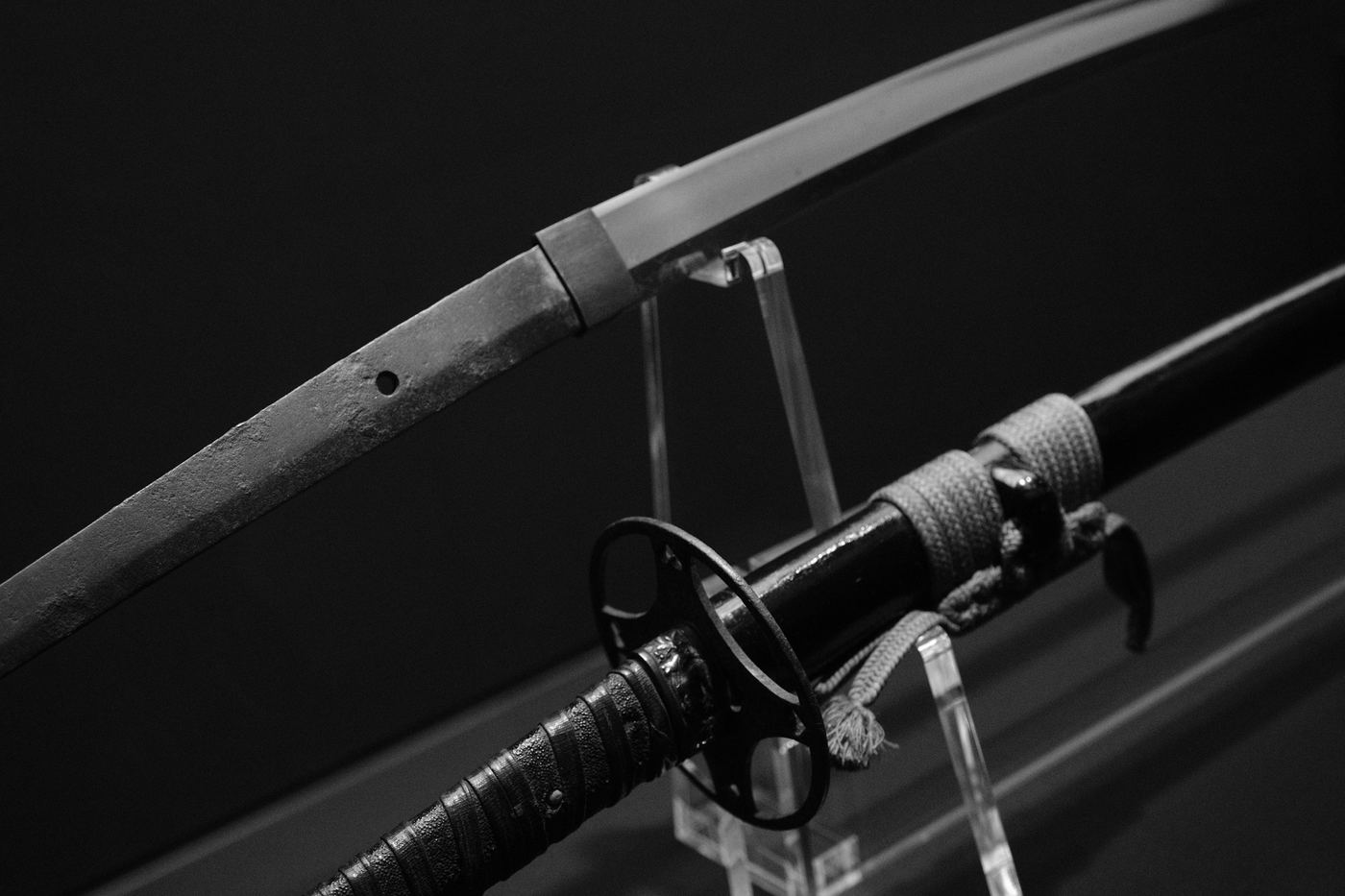 A Japanese sword resting on a clear stand, in black and white