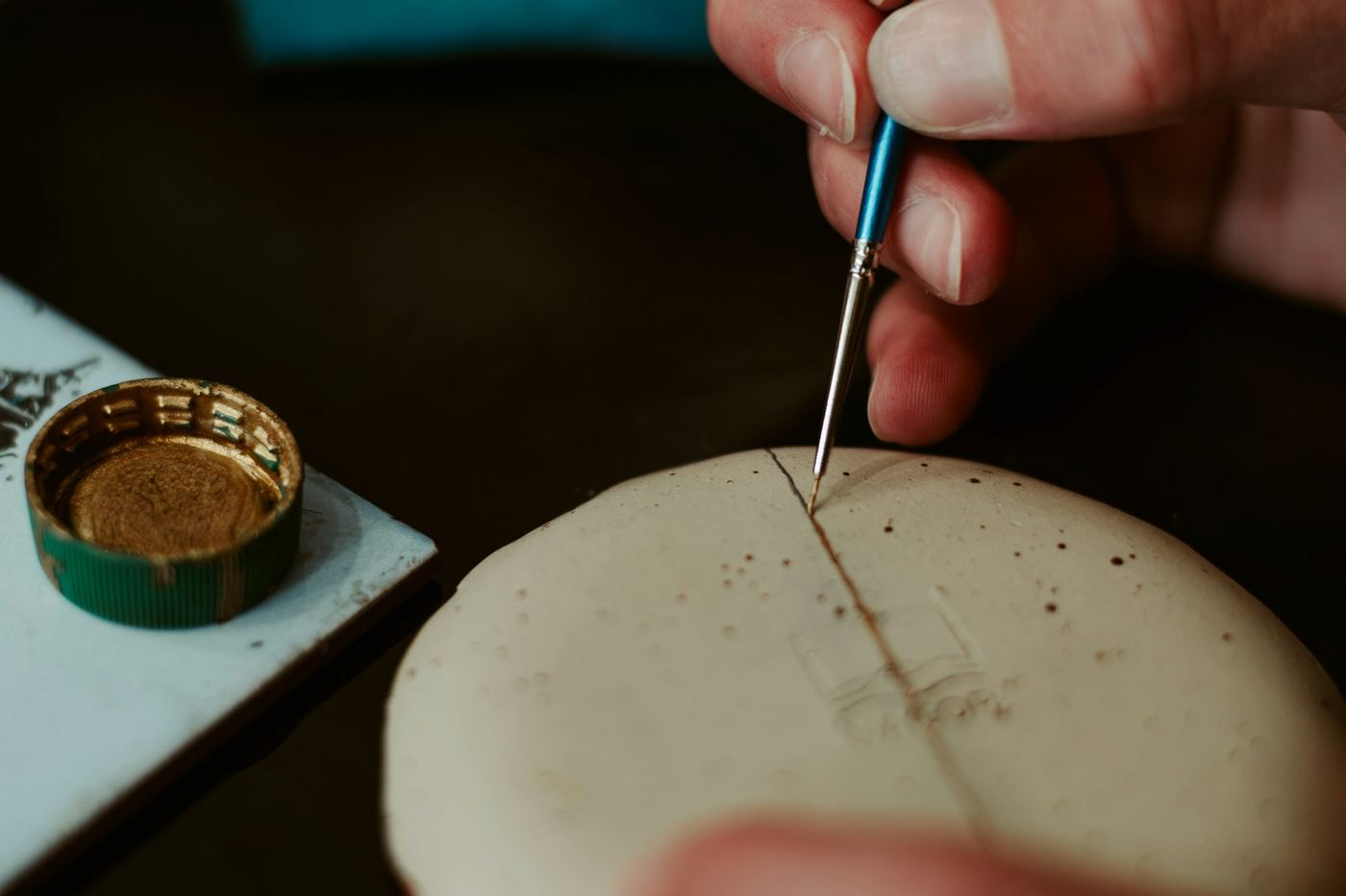A hand drawing a fine line along a crack in a pale dish