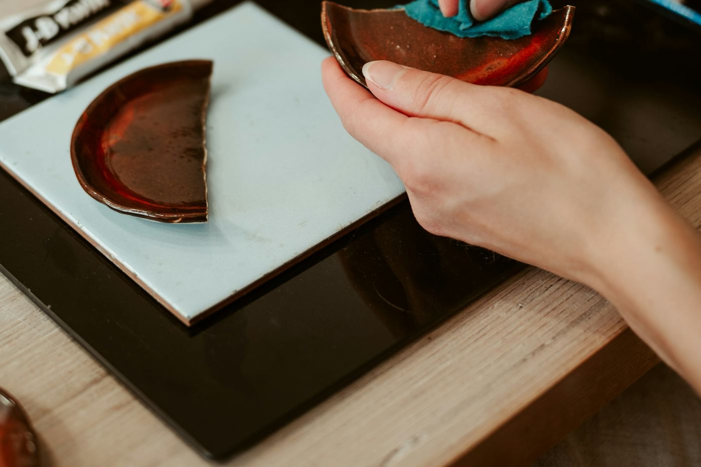 Hands wiping a broken lacquered bowl at a work table