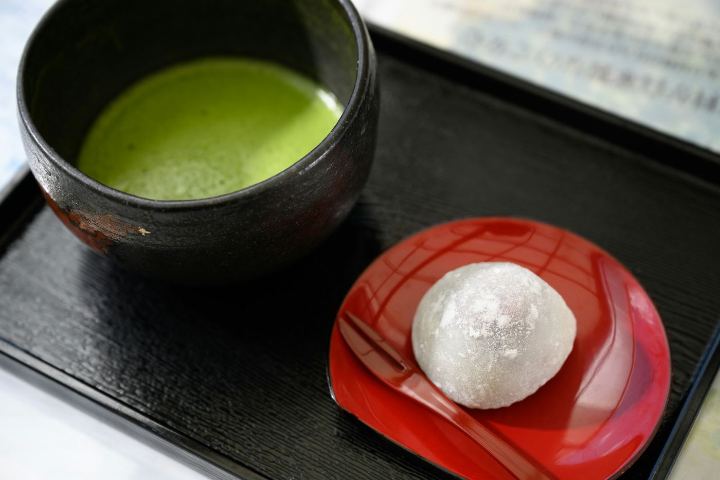 A bowl of matcha beside a white sweet on a red dish