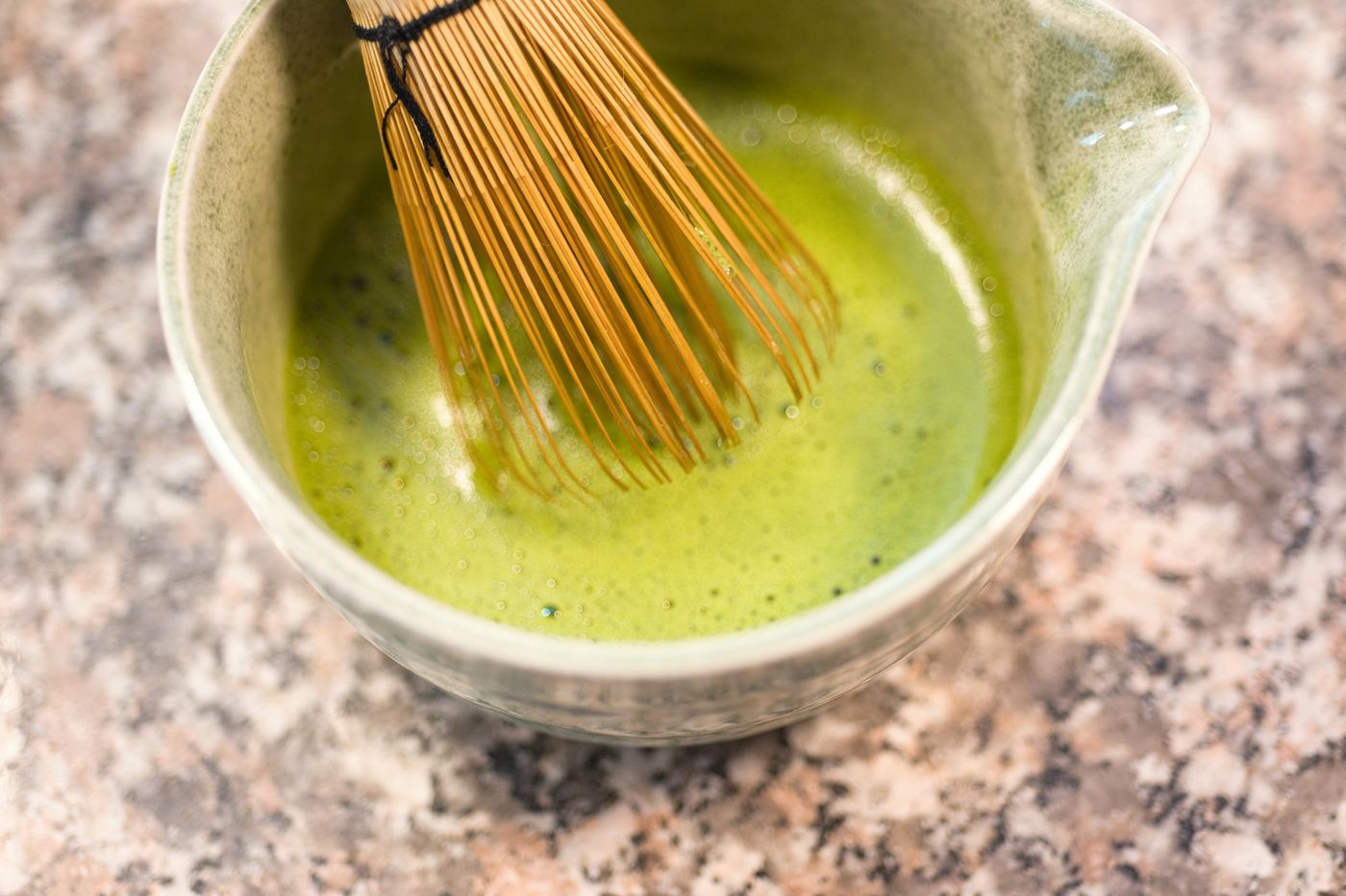 A bamboo whisk in a bowl of bright green matcha