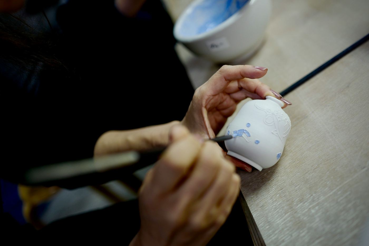 Hands painting a pattern on a small white cup with a fine brush