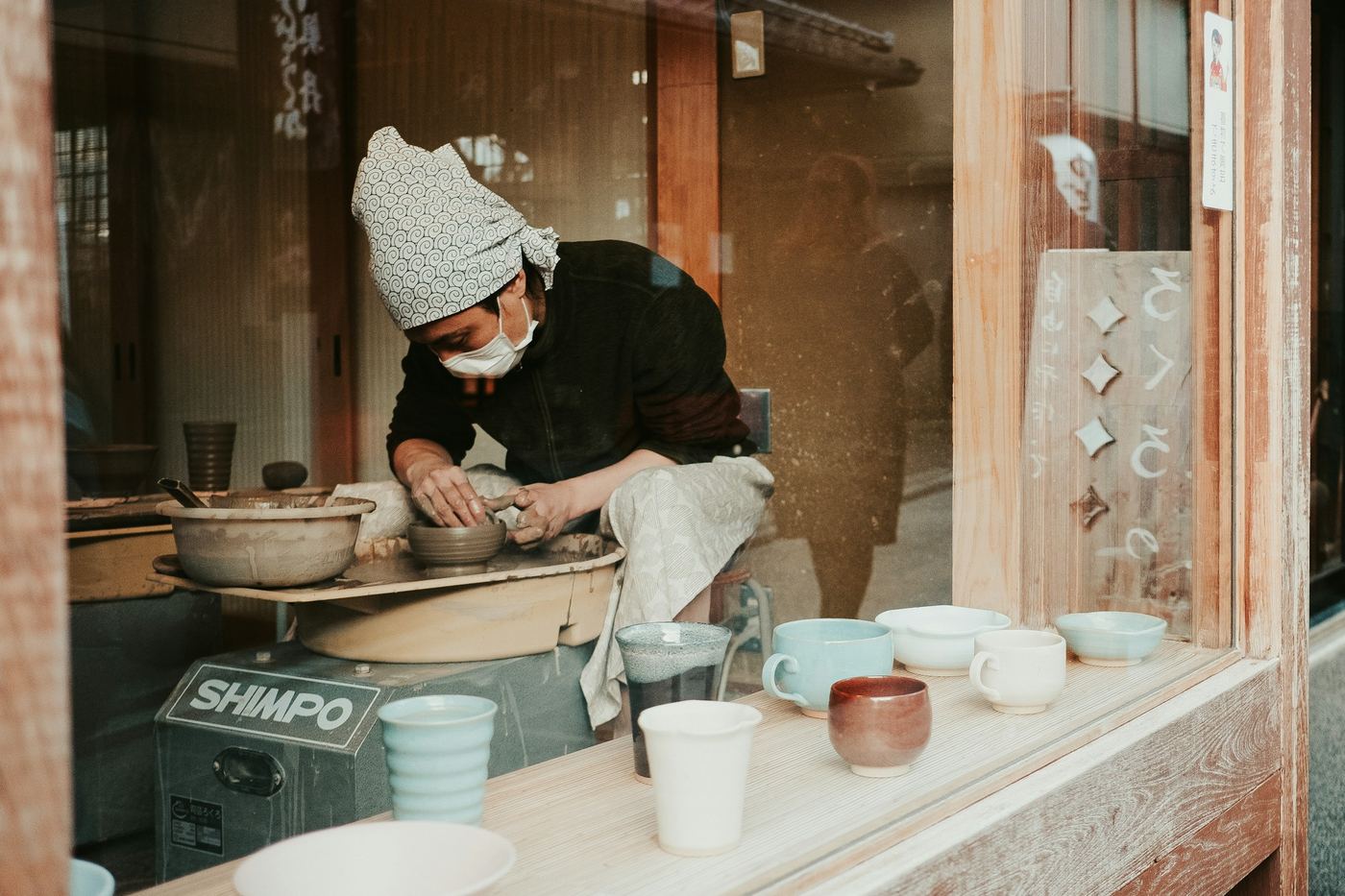 A potter at the wheel in a workshop open to the street