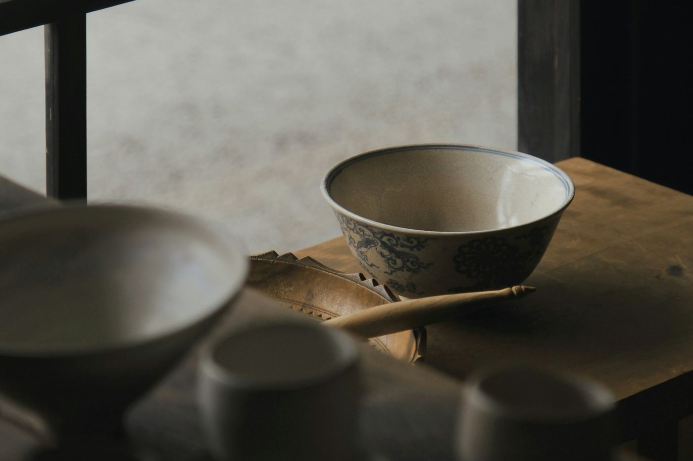 Ceramic bowls and cups on a wooden table by a window