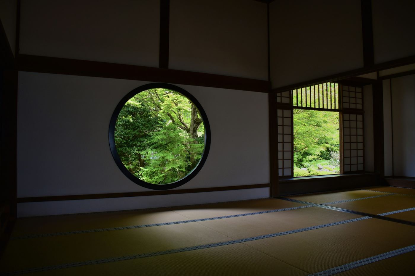A round window in a tatami room looking onto green trees