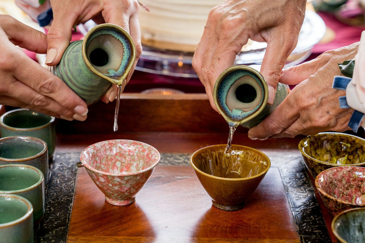 Hands pouring sake from flasks into small cups