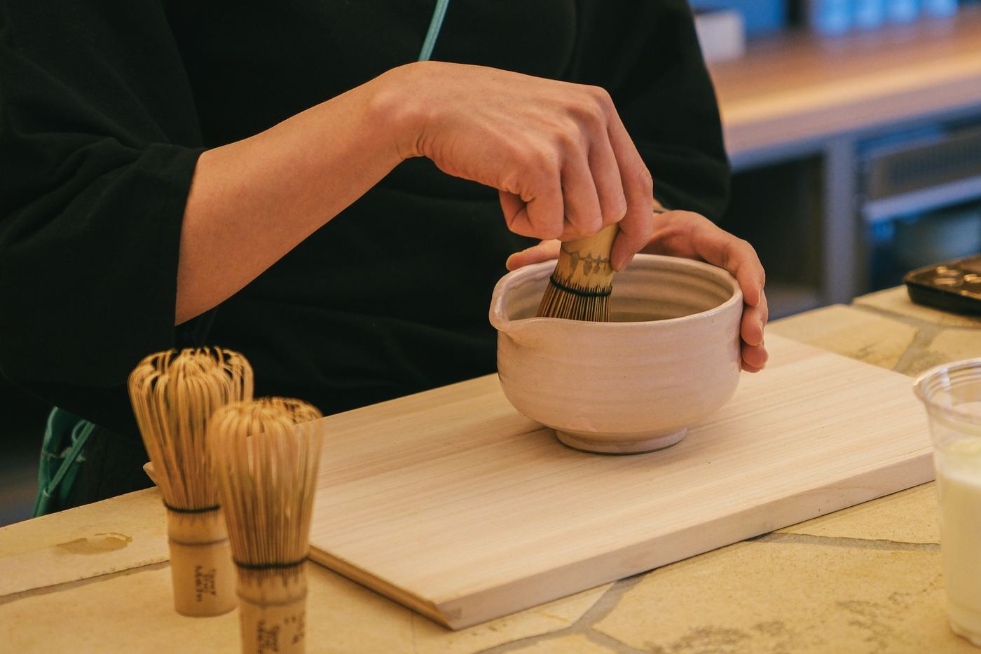 Hands whisking matcha in a ceramic bowl