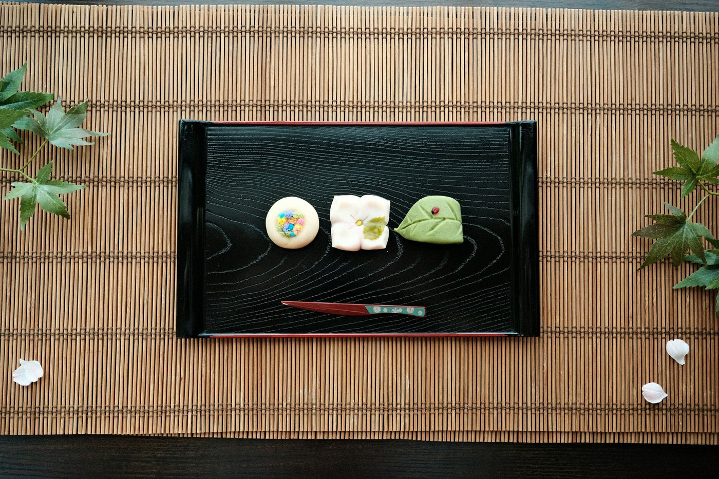 Three small sweets on a black lacquer tray on a bamboo mat