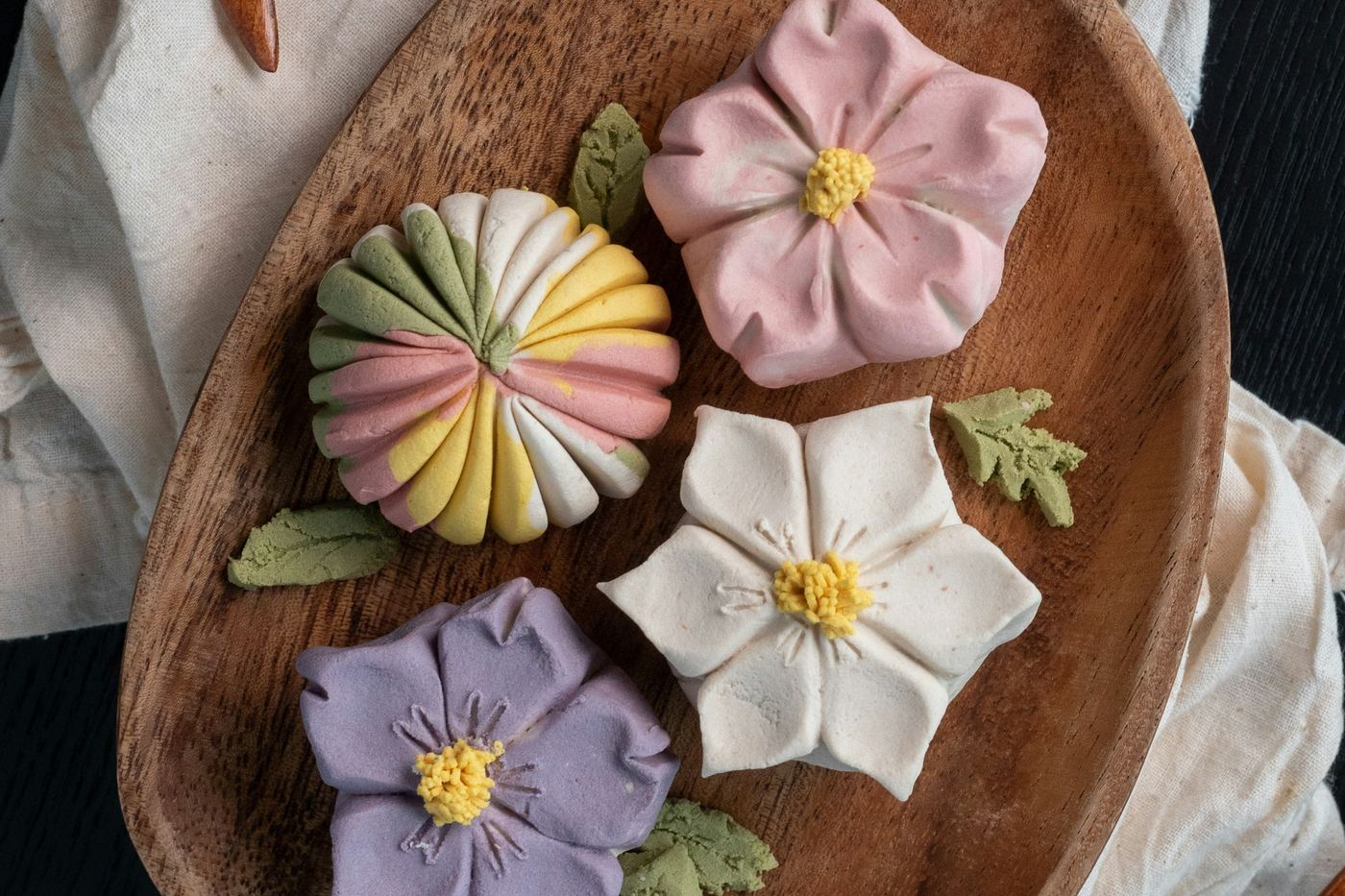 Flower-shaped Japanese sweets in purple, pink and white on a wooden plate