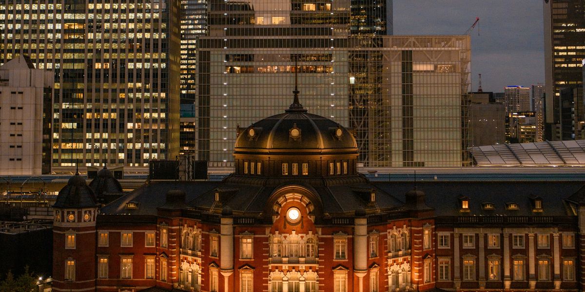 La fachada de ladrillo rojo de la estación de Tokio iluminada al anochecer, bajo las torres de Marunouchi