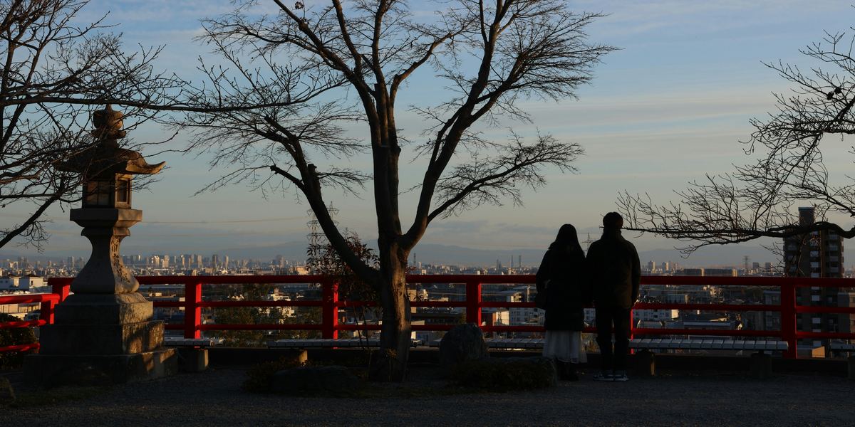 Two people standing side by side at a temple lookout, watching the evening sky over the city