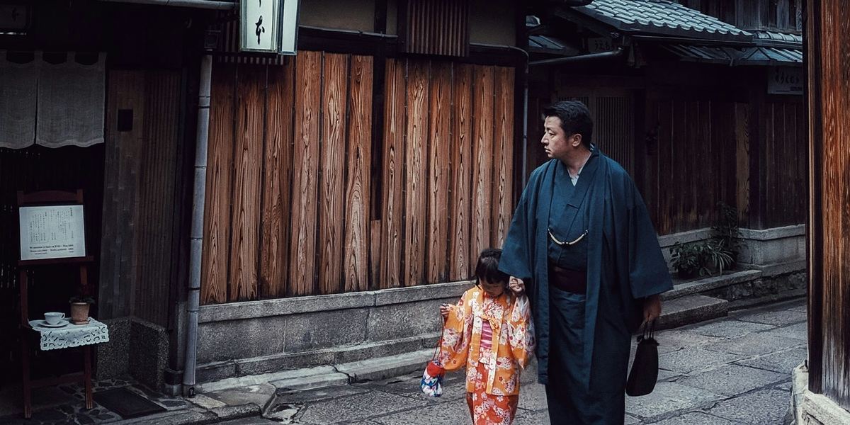A father and a small child in kimono walking past wooden houses in Higashiyama, Kyoto