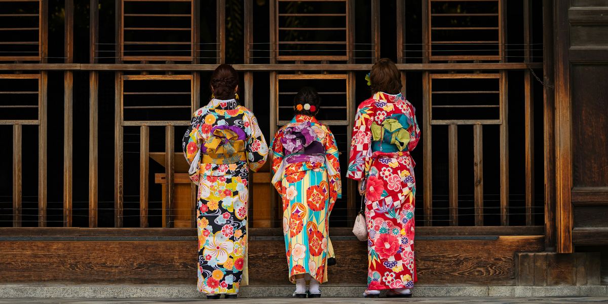 京都のお寺の木の門の前に並んで立つ、色鮮やかな着物の三人の後ろ姿