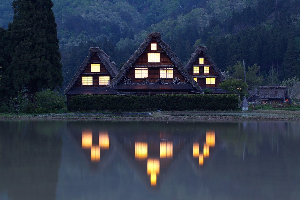 Gassho farmhouses lit at dusk, mirrored in still water