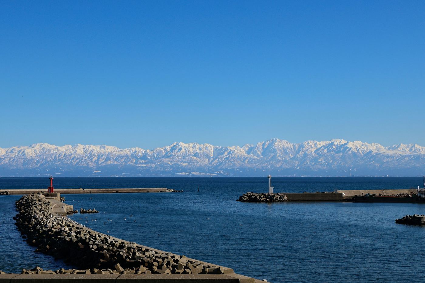 Snow-capped mountains rising beyond a calm blue sea in Toyama