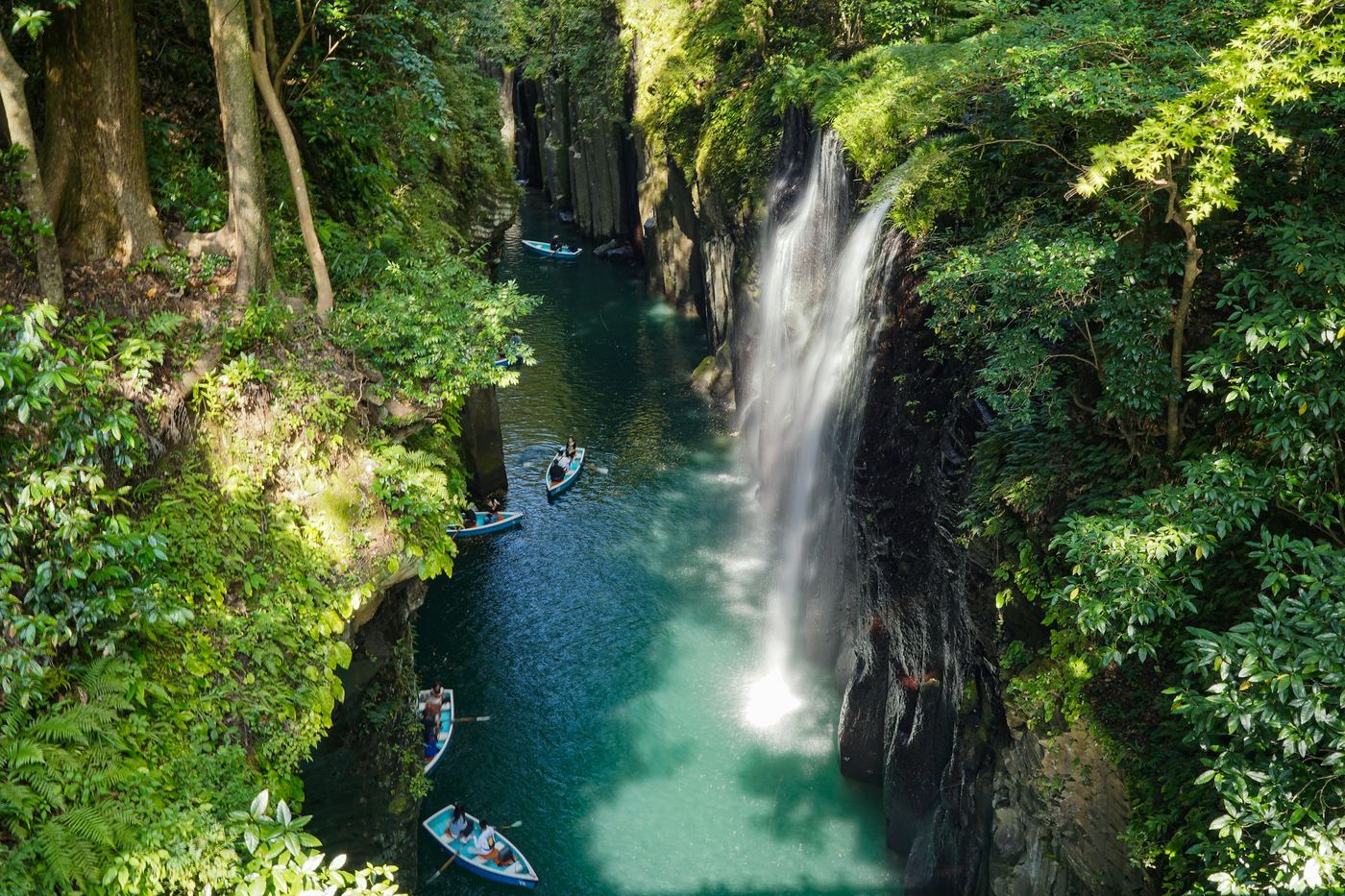 A waterfall dropping into the turquoise river of Takachiho Gorge, with rowing boats below