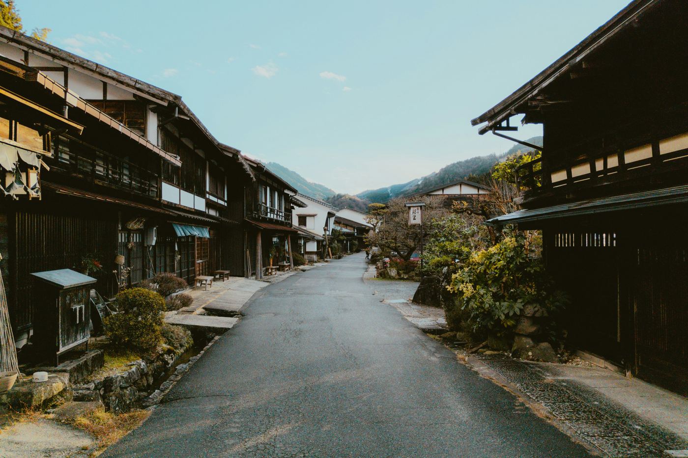 The main street of Tsumago, lined with dark wooden inns and houses, with wooded hills beyond