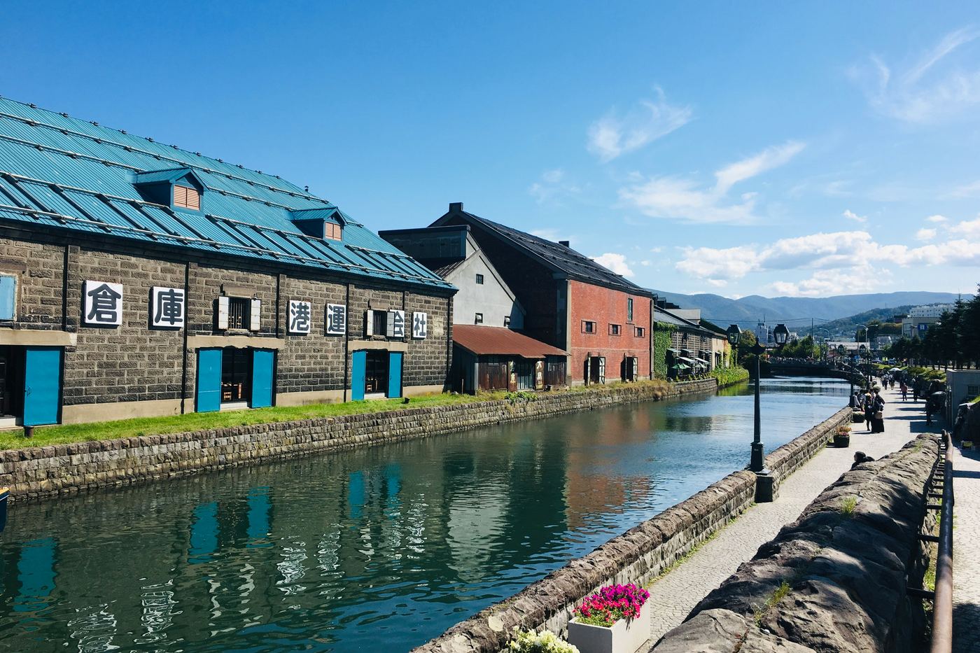 Stone warehouses with blue roofs along the Otaru Canal under a clear sky